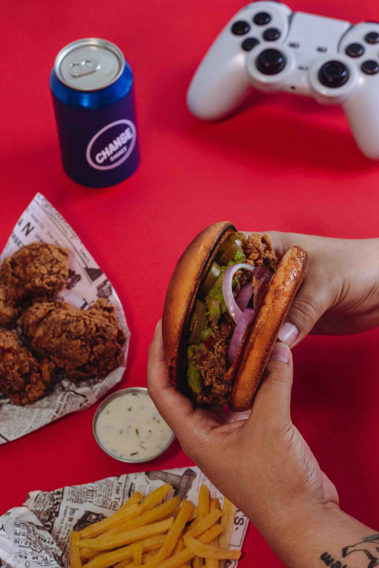 A crispy chicken burger, fries, wings and a drink beside a game controller
